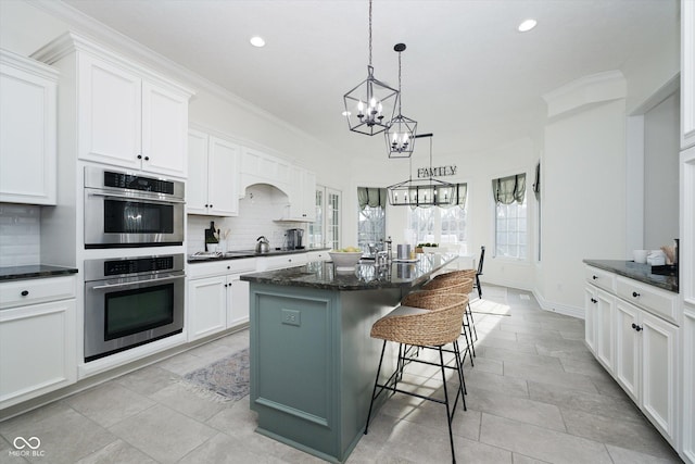 kitchen featuring a breakfast bar, a kitchen island with sink, white cabinetry, decorative backsplash, and stainless steel double oven