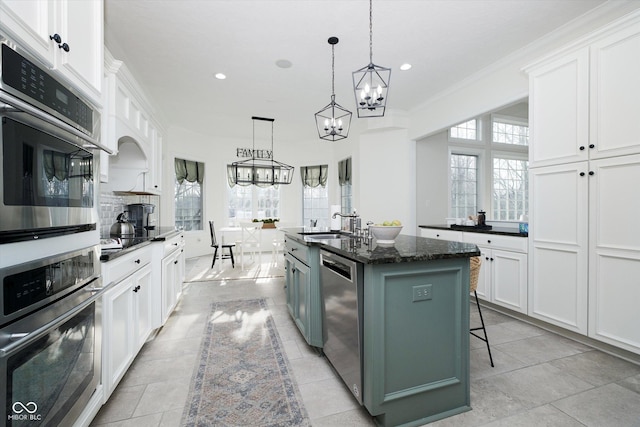 kitchen with appliances with stainless steel finishes, white cabinets, a kitchen bar, hanging light fixtures, and a center island with sink