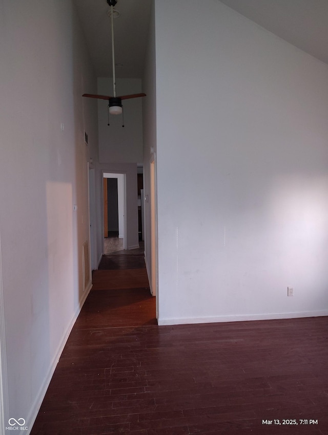 hall featuring a towering ceiling, visible vents, baseboards, and wood finished floors