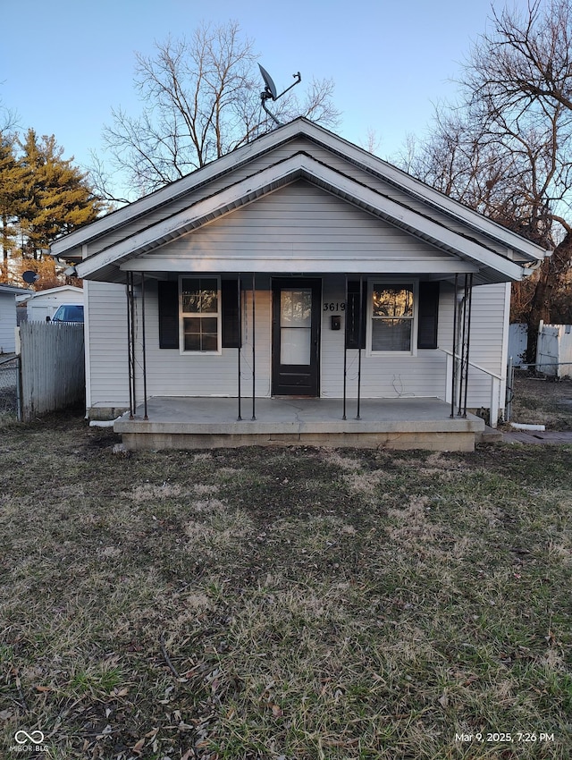 bungalow-style home with covered porch, a front yard, and fence