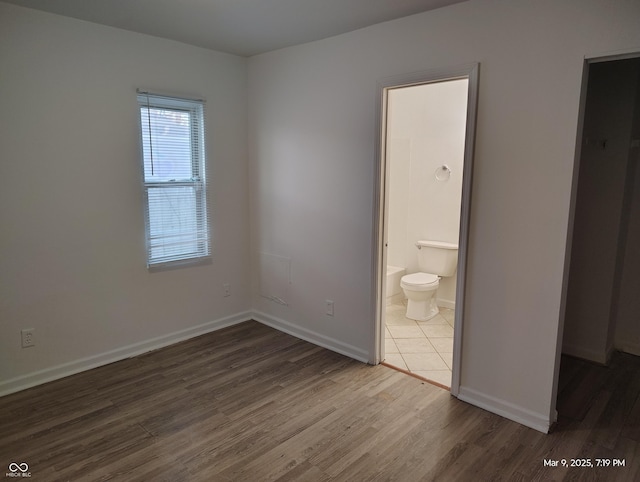 unfurnished bedroom featuring connected bathroom, baseboards, and wood finished floors