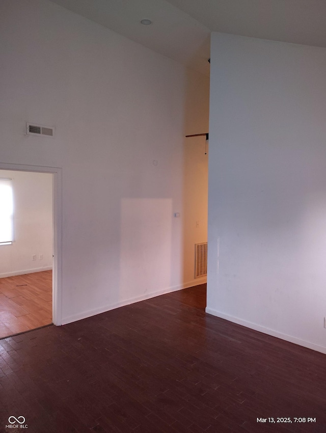 spare room featuring wood finished floors, visible vents, a towering ceiling, and baseboards