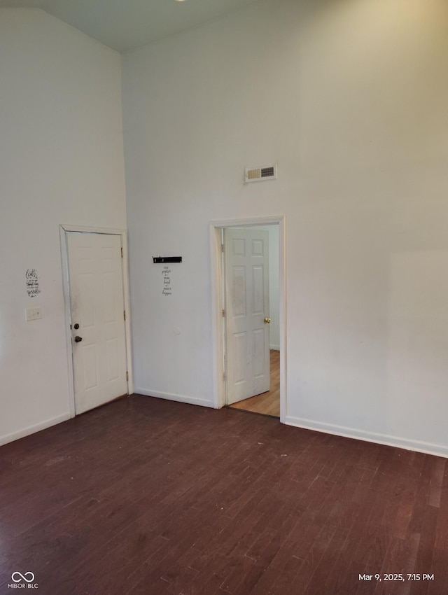 empty room with baseboards, wood finished floors, visible vents, and a towering ceiling