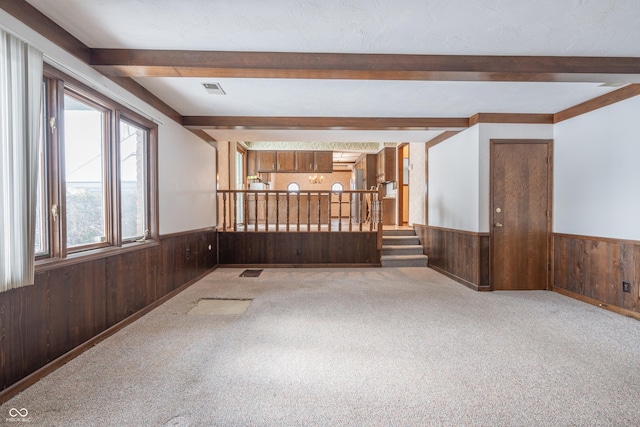 empty room with beam ceiling, wooden walls, and light colored carpet