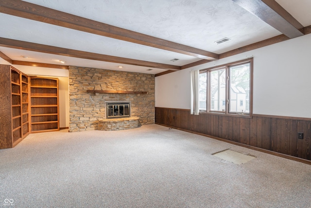 unfurnished living room featuring a textured ceiling, a fireplace, beamed ceiling, and wood walls