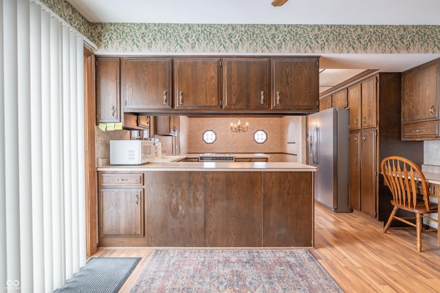 kitchen featuring dark brown cabinetry, kitchen peninsula, light hardwood / wood-style floors, and stainless steel fridge with ice dispenser