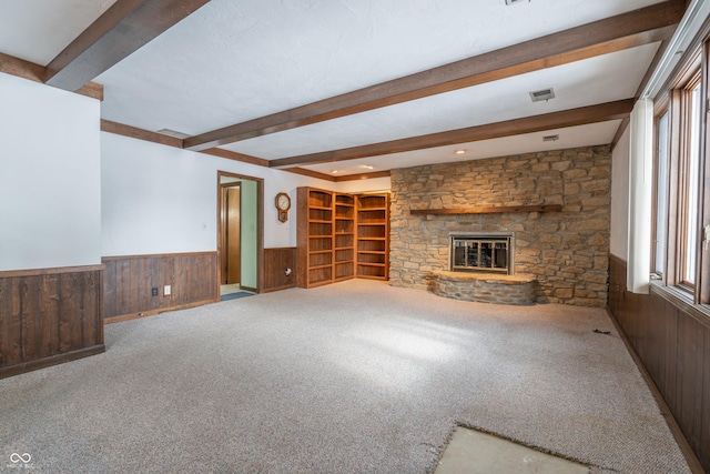 unfurnished living room featuring light carpet, a fireplace, beam ceiling, and wood walls