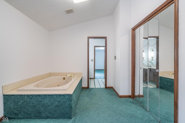 bathroom with lofted ceiling, vanity, tiled bath, and a textured ceiling