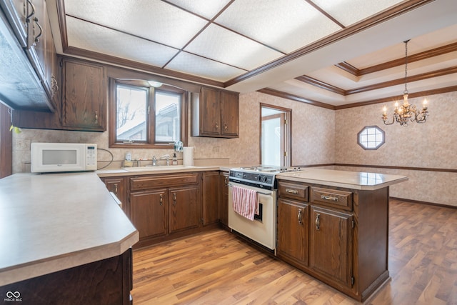 kitchen with sink, white appliances, light hardwood / wood-style floors, decorative light fixtures, and kitchen peninsula