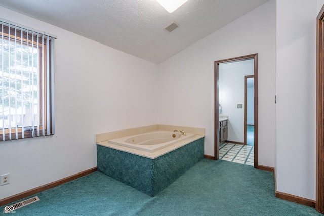 bathroom featuring a tub to relax in, lofted ceiling, a textured ceiling, and plenty of natural light