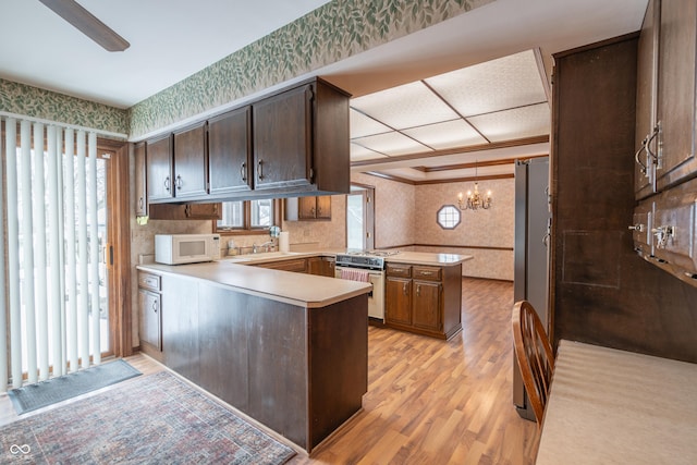 kitchen featuring sink, range, dark brown cabinetry, kitchen peninsula, and light wood-type flooring