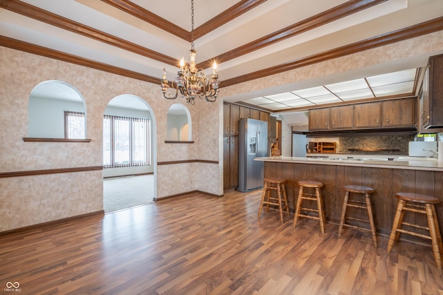 kitchen with stainless steel fridge with ice dispenser, ornamental molding, dark hardwood / wood-style flooring, kitchen peninsula, and a notable chandelier