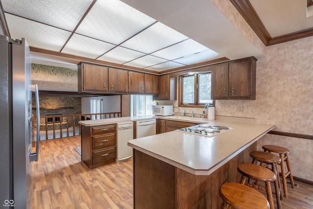 kitchen featuring a breakfast bar, ornamental molding, kitchen peninsula, stainless steel appliances, and light hardwood / wood-style flooring