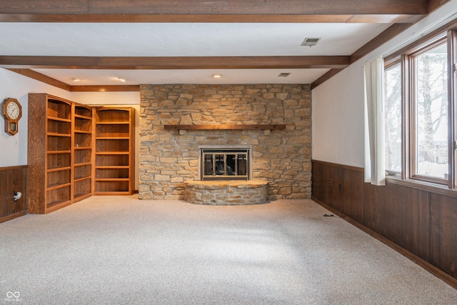 unfurnished living room with beamed ceiling, carpet flooring, a fireplace, and wood walls