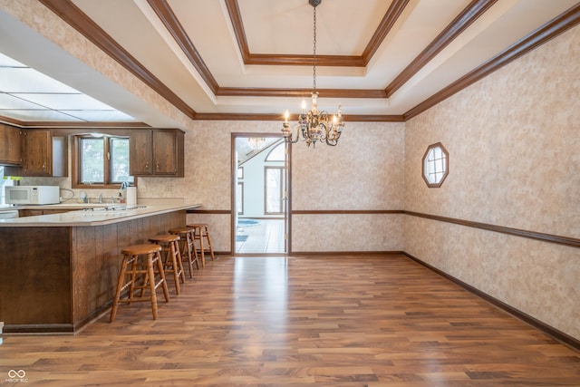 kitchen with ornamental molding, a kitchen breakfast bar, dark hardwood / wood-style flooring, kitchen peninsula, and a tray ceiling