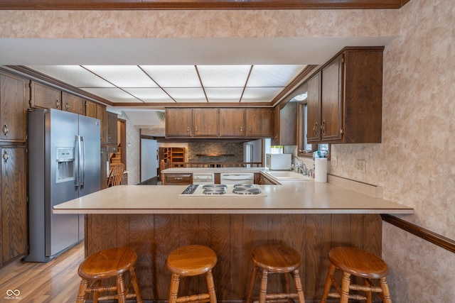 kitchen with sink, stainless steel fridge, a kitchen bar, kitchen peninsula, and light wood-type flooring