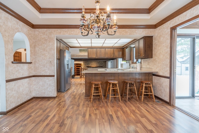 kitchen with a kitchen bar, wood-type flooring, a tray ceiling, stainless steel fridge, and kitchen peninsula