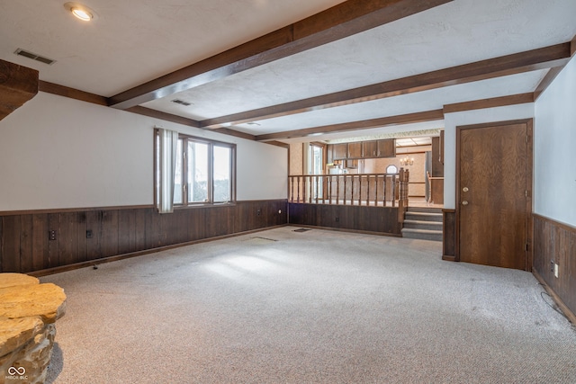 interior space featuring beamed ceiling, wooden walls, light carpet, and a textured ceiling