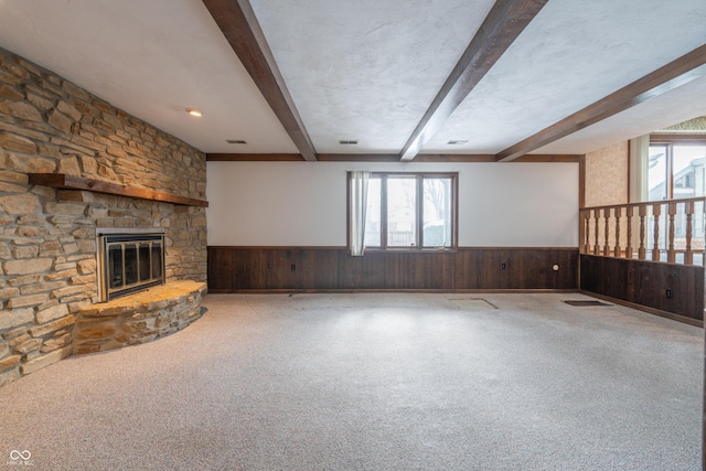 unfurnished living room with wooden walls, a fireplace, a healthy amount of sunlight, and beam ceiling