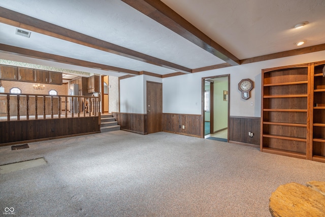 unfurnished living room featuring beamed ceiling, carpet floors, and wooden walls