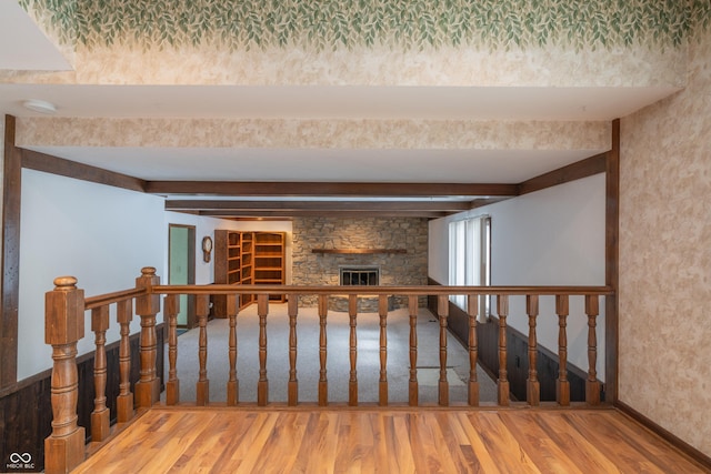 stairway with hardwood / wood-style flooring, a stone fireplace, and beamed ceiling