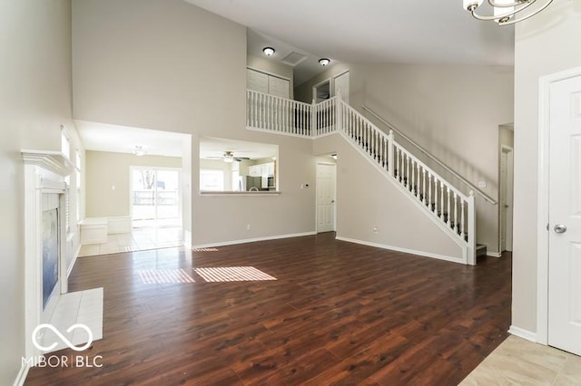 unfurnished living room with dark wood-type flooring, ceiling fan, a premium fireplace, and a high ceiling