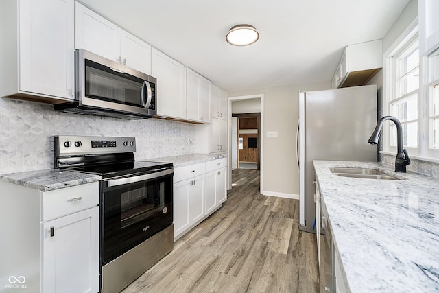 kitchen with tasteful backsplash, light wood-type flooring, appliances with stainless steel finishes, light stone countertops, and white cabinets