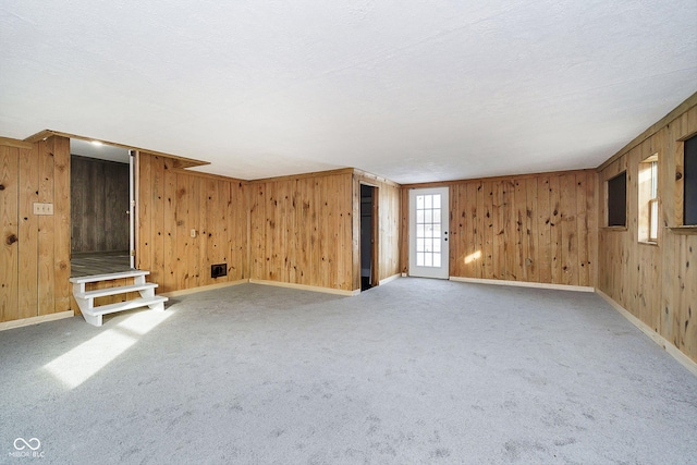 unfurnished living room with carpet floors, wooden walls, and a textured ceiling