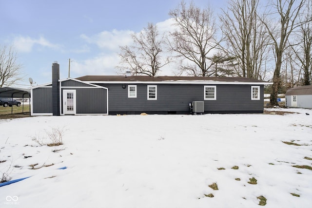 snow covered property featuring a carport, a storage unit, and central air condition unit