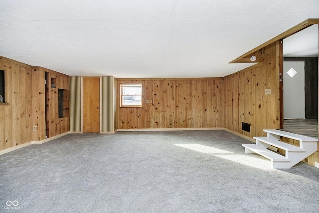 interior space featuring carpet flooring, a textured ceiling, and wood walls