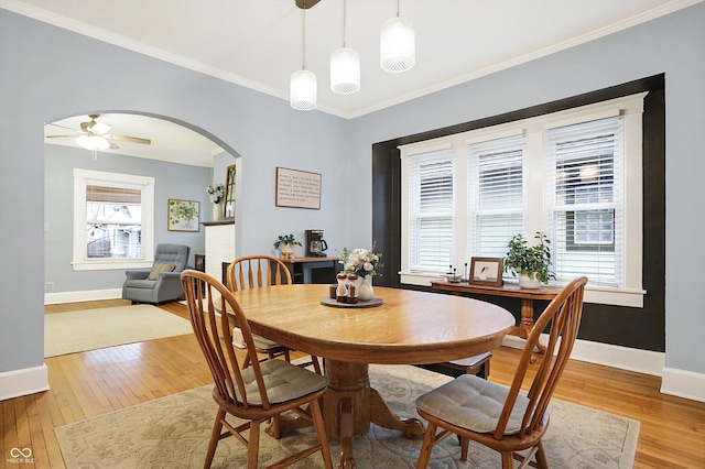 dining area with ornamental molding, arched walkways, light wood-style flooring, and baseboards