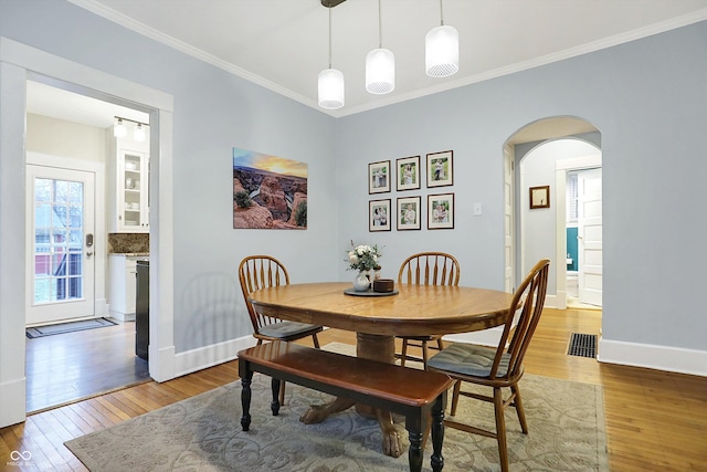 dining space with arched walkways, hardwood / wood-style floors, visible vents, and baseboards