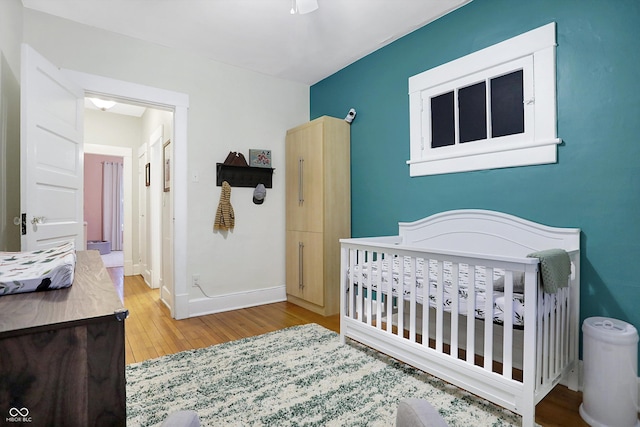 bedroom with a nursery area, mail area, baseboards, and wood finished floors