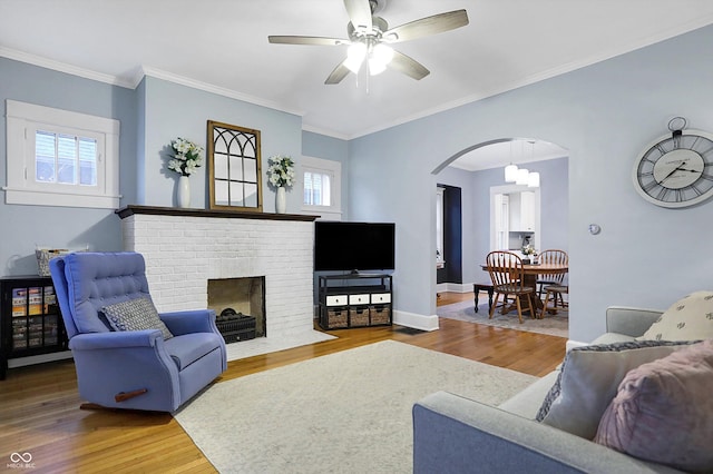 living room featuring baseboards, arched walkways, ceiling fan, wood finished floors, and a fireplace