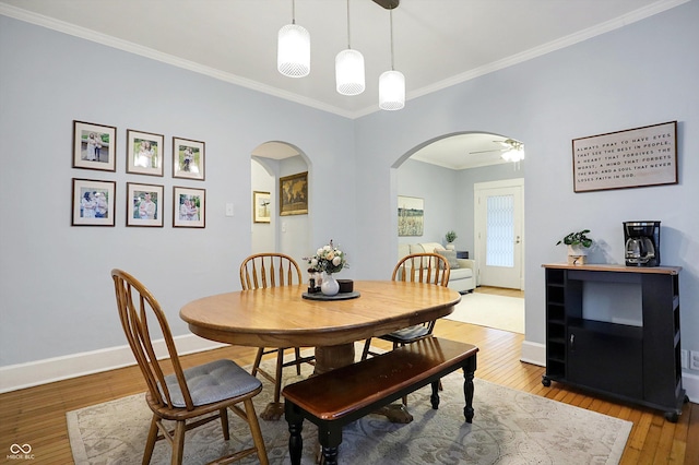 dining area with light wood finished floors, baseboards, arched walkways, and crown molding