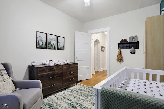 bedroom featuring arched walkways, light wood-style flooring, and baseboards