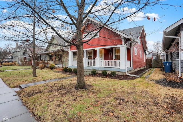 bungalow-style house featuring covered porch, fence, and a front lawn