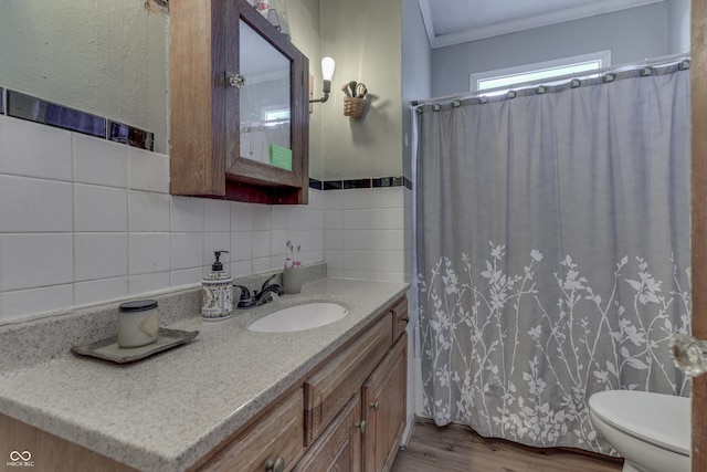 bathroom with toilet, crown molding, wood-type flooring, tile walls, and vanity