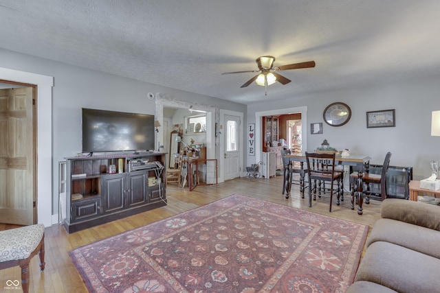 living room with ceiling fan, a textured ceiling, and light hardwood / wood-style floors