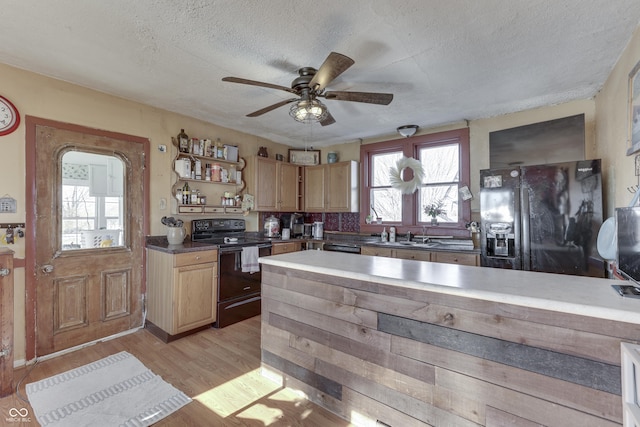 kitchen with light brown cabinetry, black appliances, light hardwood / wood-style floors, and a textured ceiling