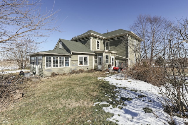 snow covered rear of property with a lawn and a sunroom