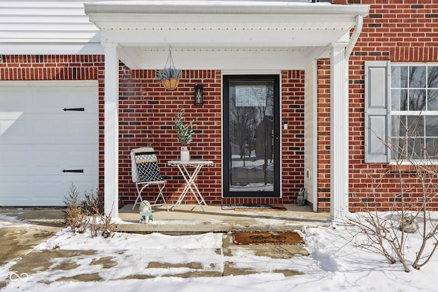 snow covered property entrance with an attached garage and brick siding