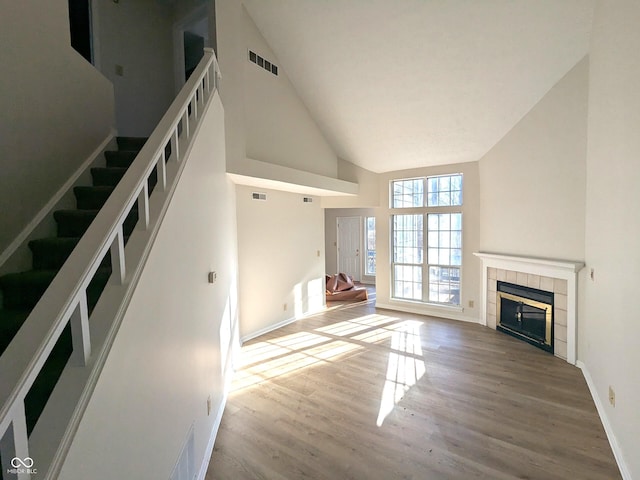 unfurnished living room featuring a tile fireplace, hardwood / wood-style floors, and high vaulted ceiling