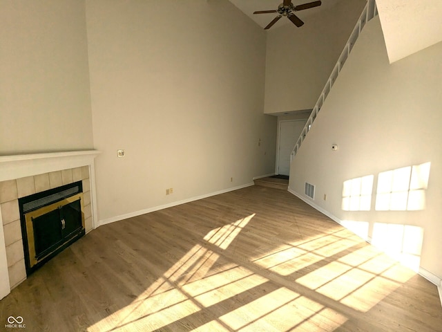 unfurnished living room with a tiled fireplace, a high ceiling, ceiling fan, and light wood-type flooring