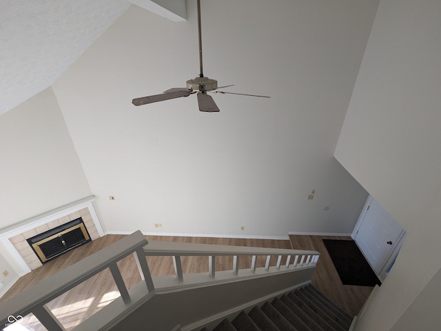 stairway featuring ceiling fan, wood-type flooring, a tiled fireplace, and high vaulted ceiling