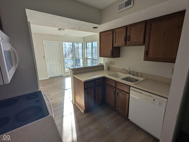 kitchen with sink, white appliances, wood-type flooring, and kitchen peninsula