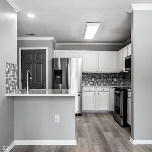 kitchen featuring appliances with stainless steel finishes, white cabinetry, decorative backsplash, kitchen peninsula, and light wood-type flooring