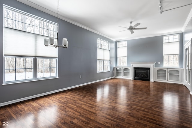 unfurnished living room with crown molding, ceiling fan with notable chandelier, dark hardwood / wood-style floors, and a wealth of natural light