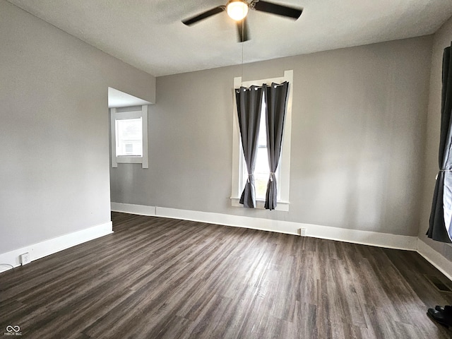 empty room with a wealth of natural light, dark wood-type flooring, and ceiling fan