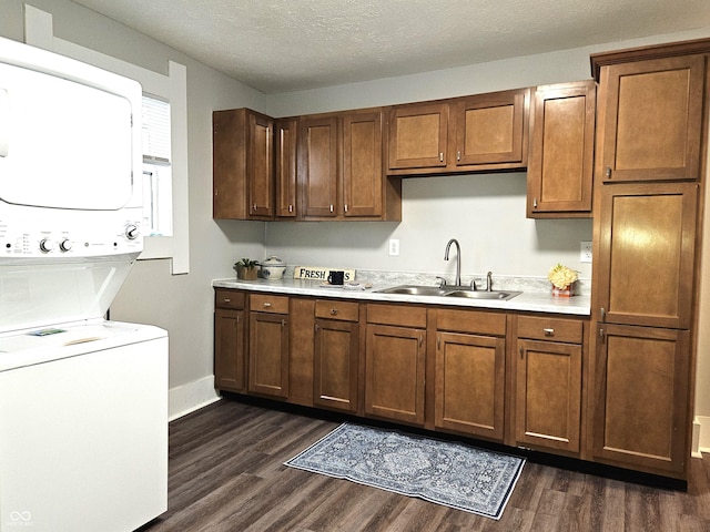 kitchen with stacked washer and dryer, sink, dark wood-type flooring, and a textured ceiling